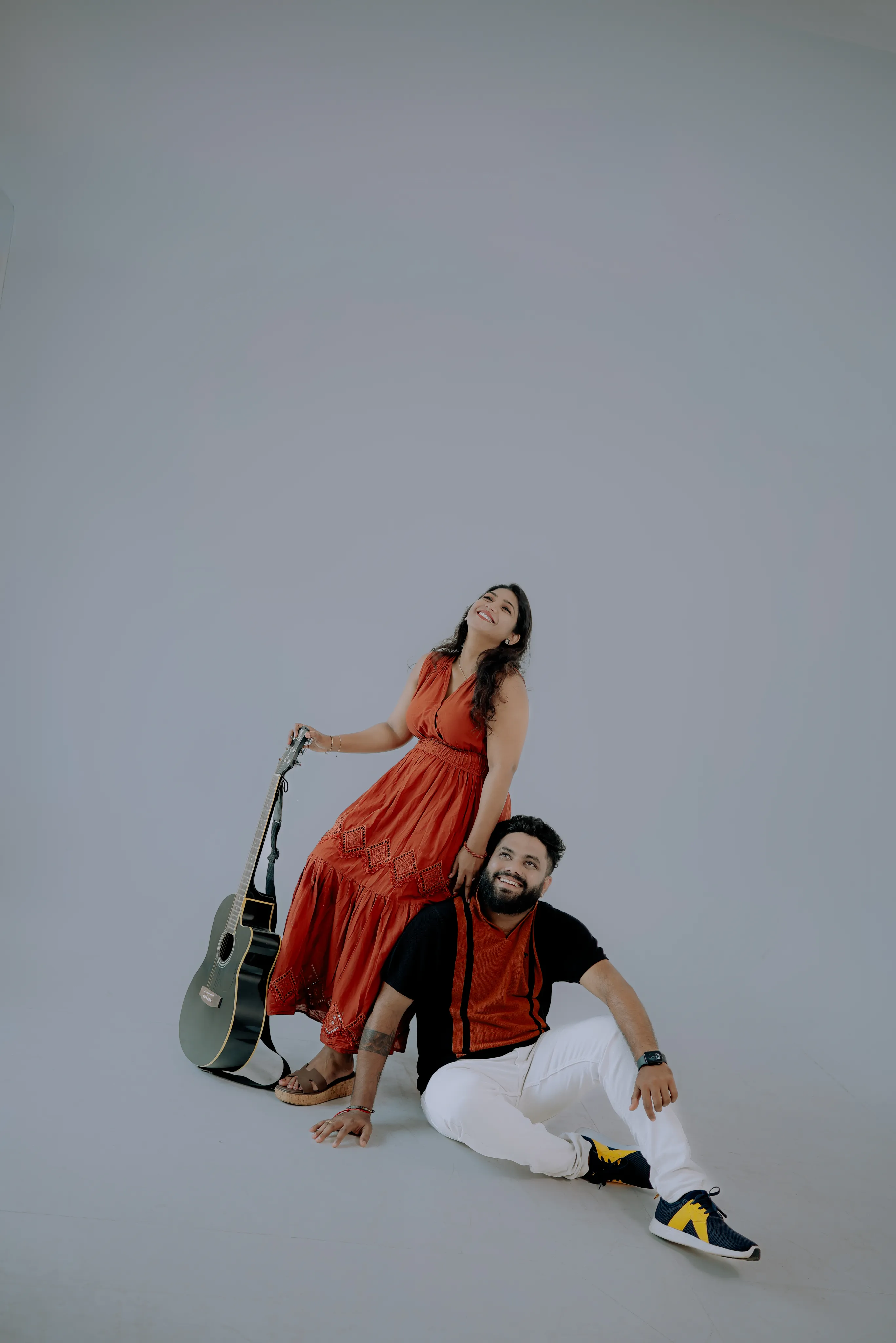 Bride laughing while leaning on the groom, who sits beside a guitar in a studio setting