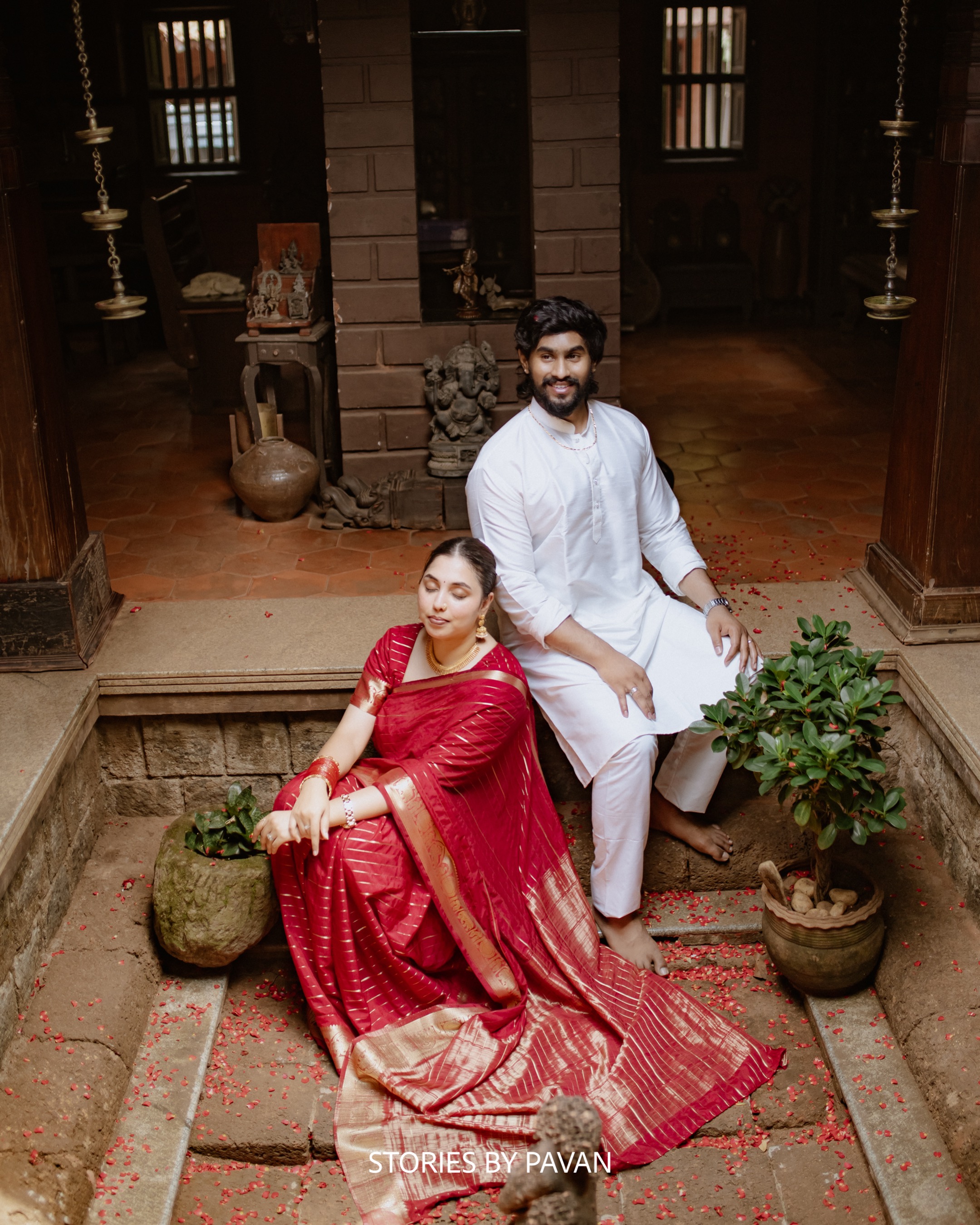 Couple seated together in a traditional Kerala courtyard, dressed in red and white