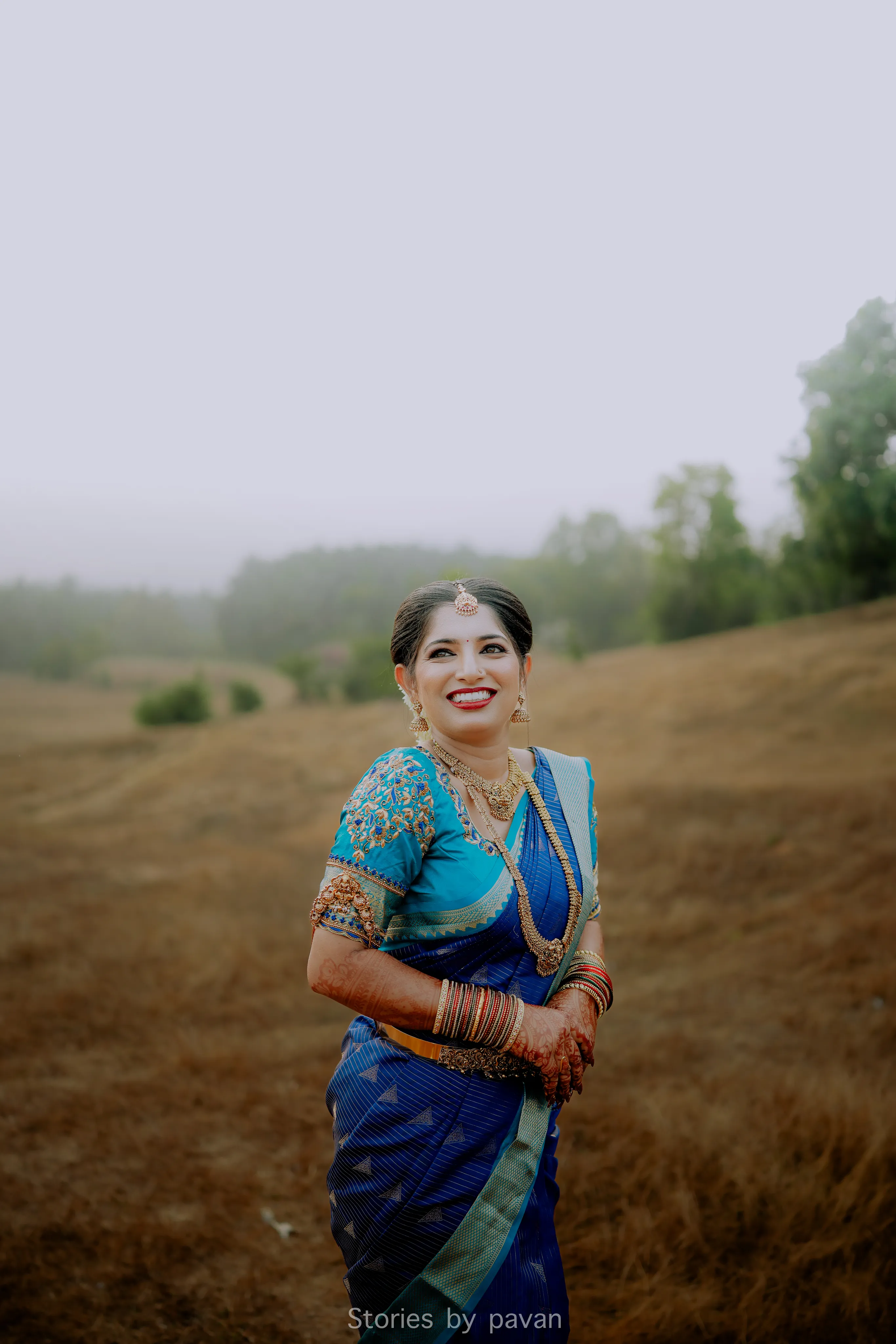 Bride in a blue and gold saree smiling in a misty open field