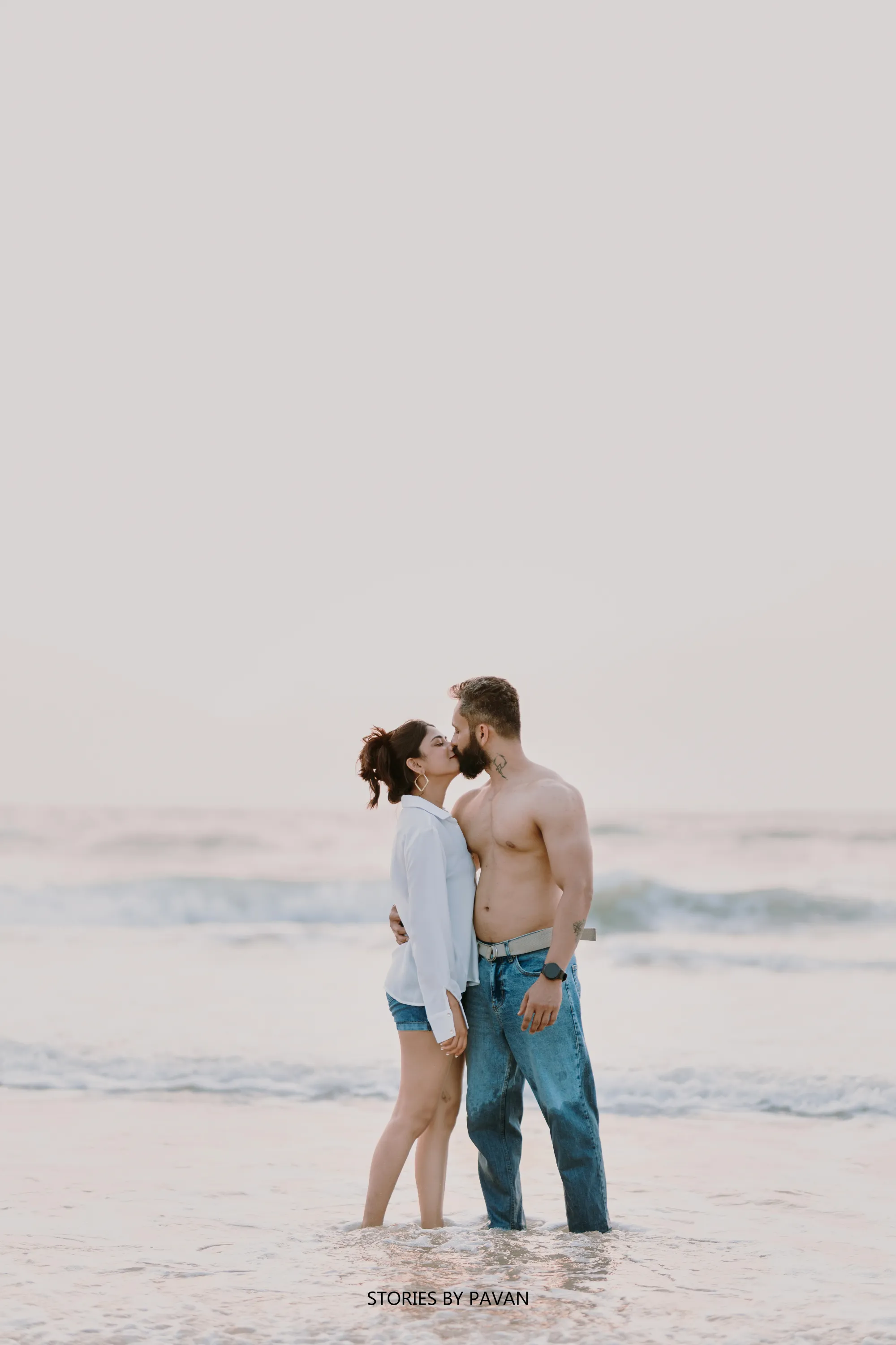 Couple sharing a kiss standing in shallow waves at the beach during golden hour