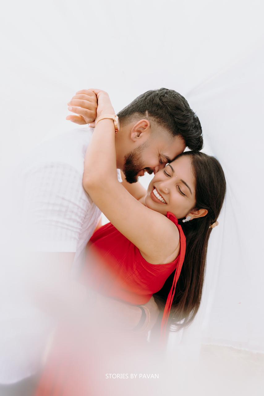 Couple embracing forehead to forehead, bride laughing, softly lit against a white backdrop